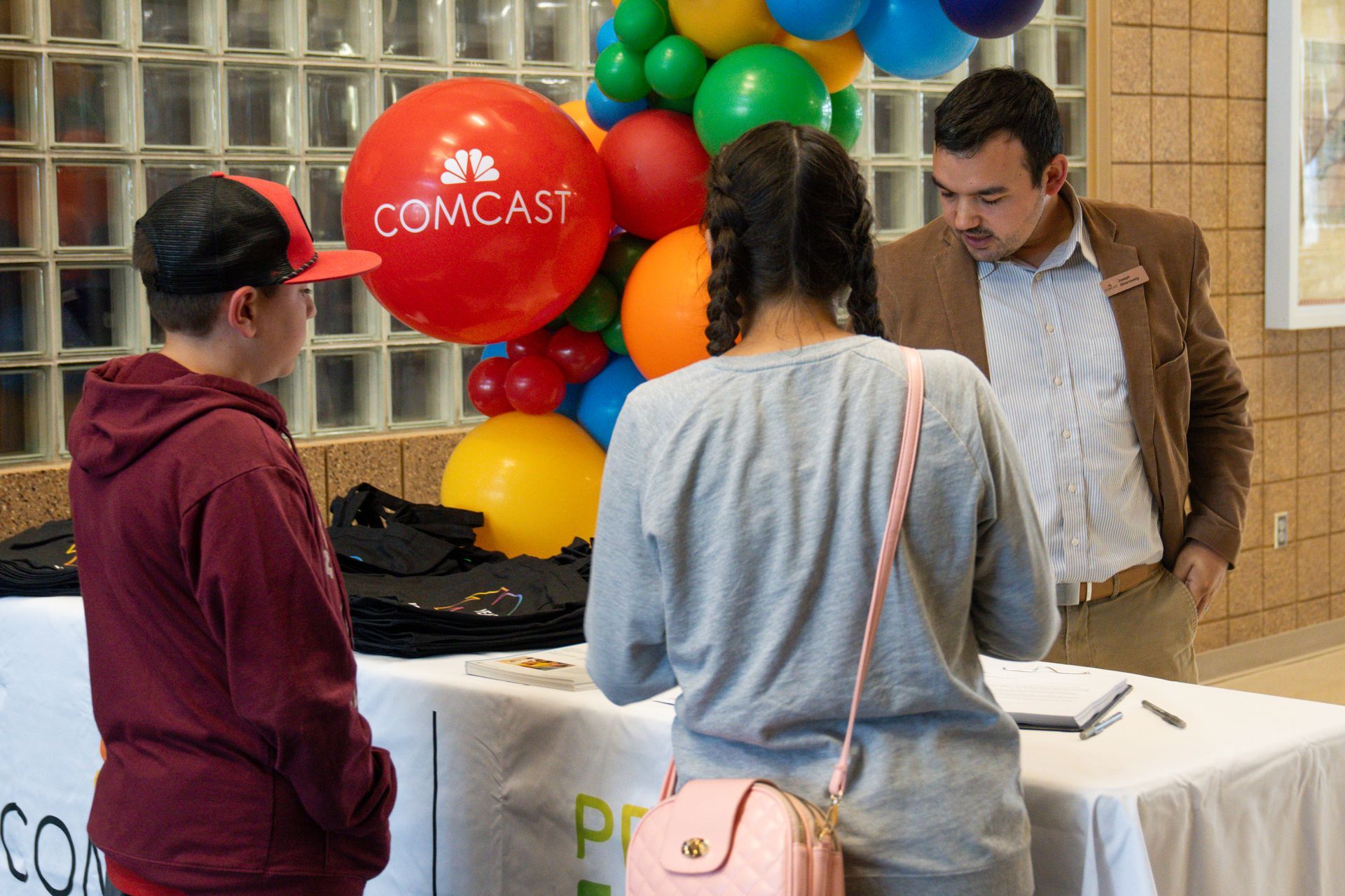 A man and two women are standing around a table with balloons and a comcast balloon in the background.