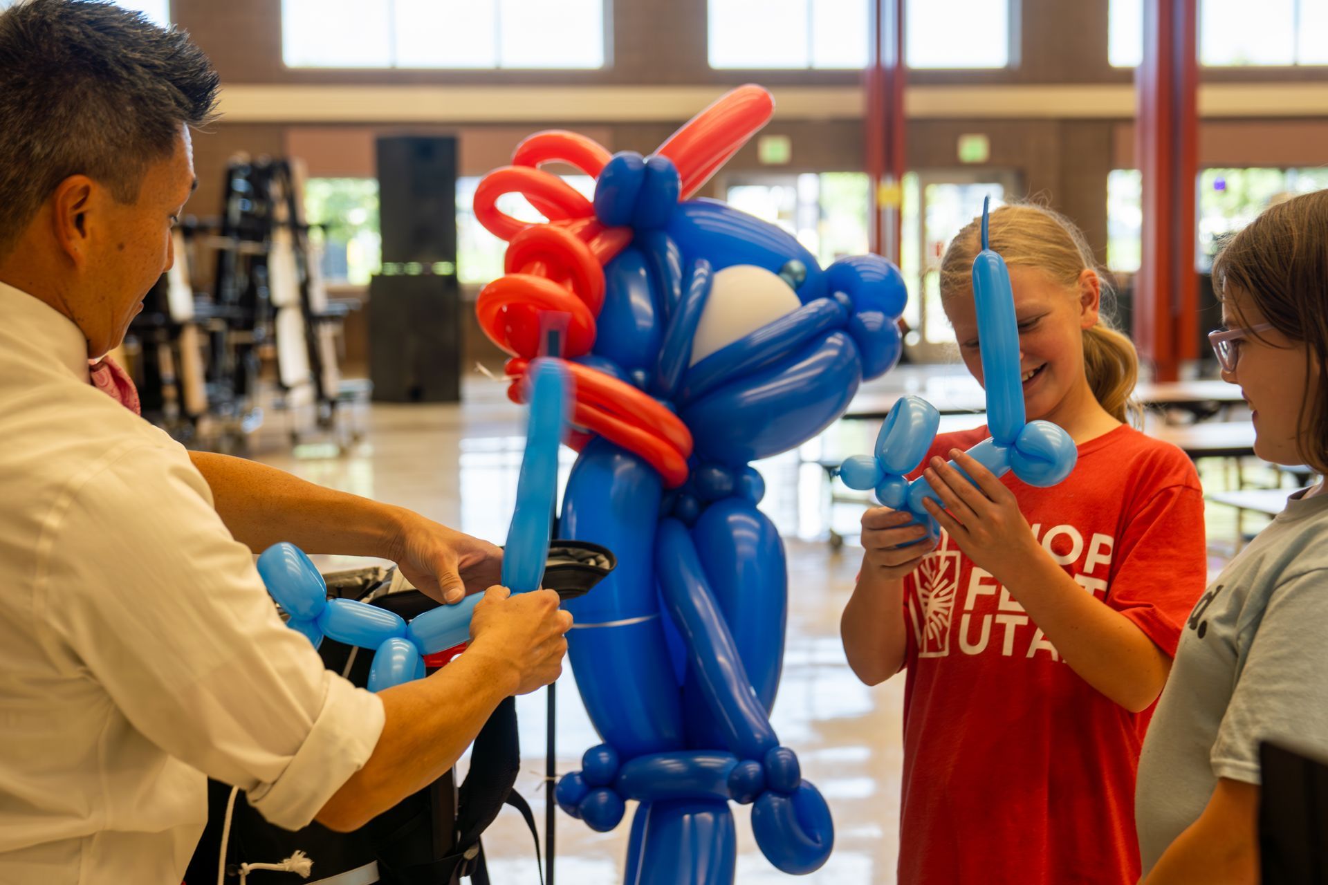 A group of children are looking at a balloon sculpture being made by a man.