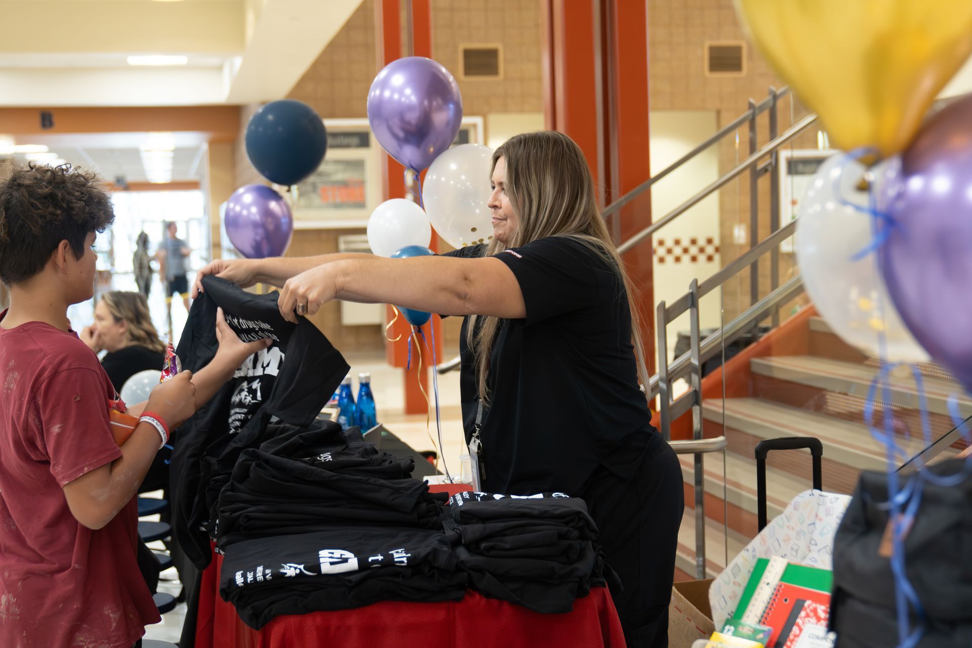 A woman is putting a shirt on a table with balloons in the background.