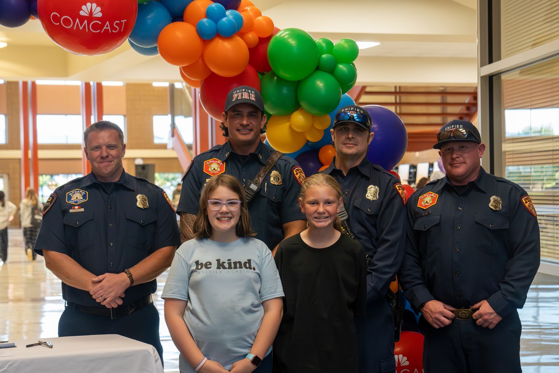 A group of firefighters and a girl are posing for a picture in front of balloons.