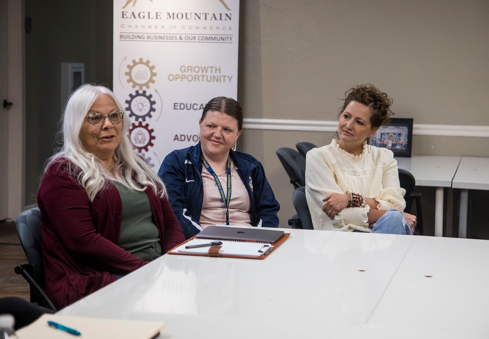 Three women are sitting at a table with a clipboard.