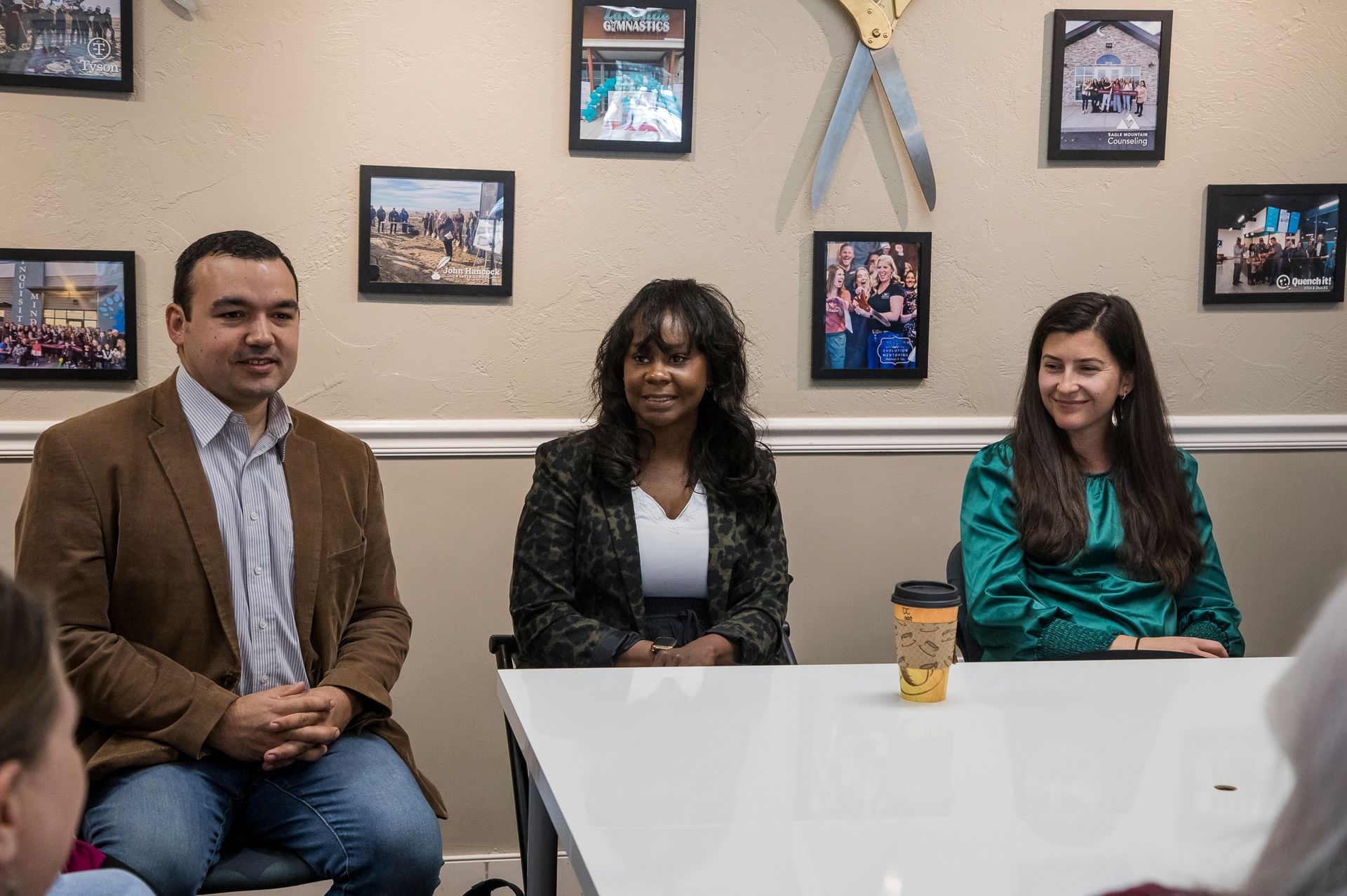 A man and two women are sitting at a table with a cup of coffee.