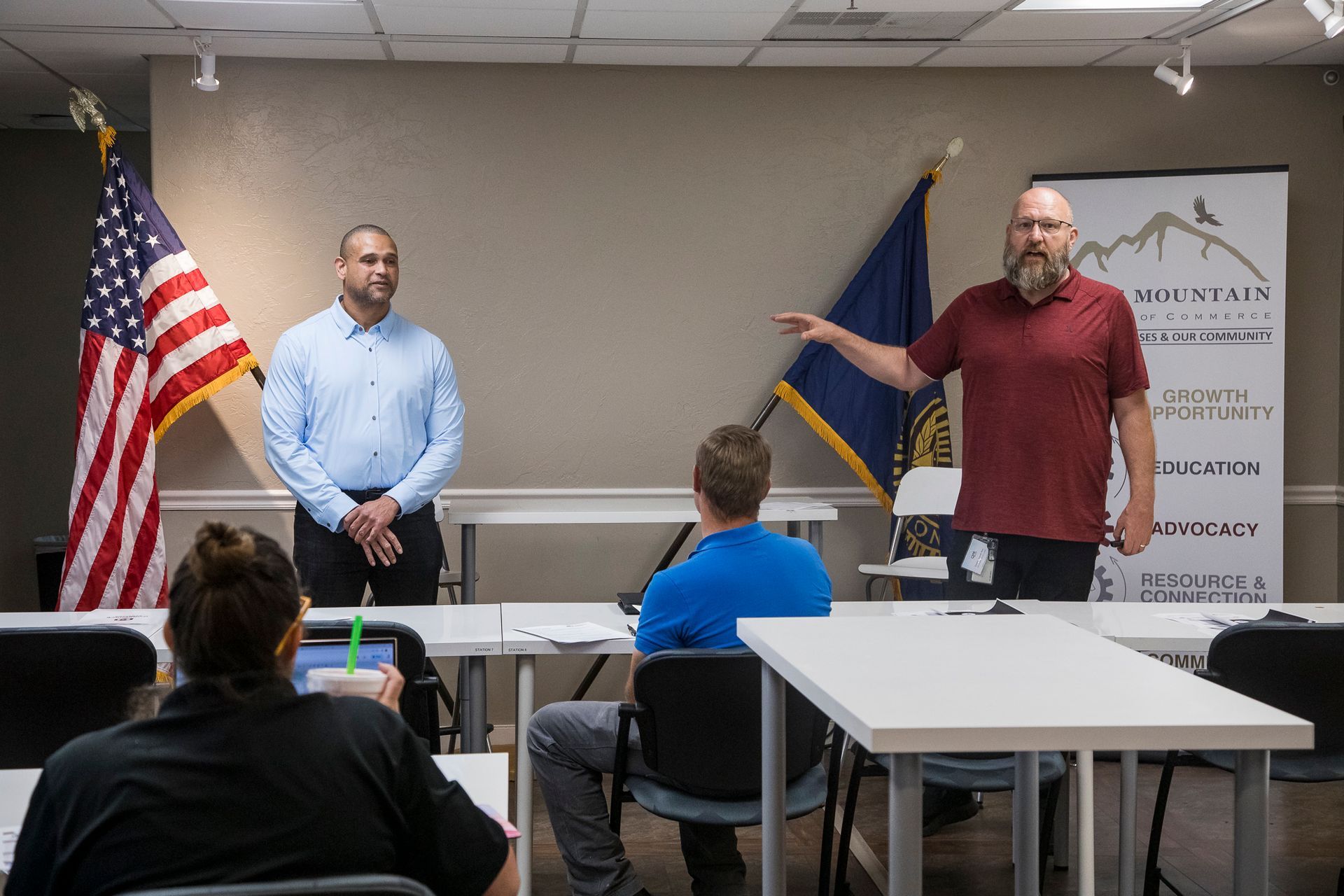 Two men are standing in front of a group of people in a classroom.