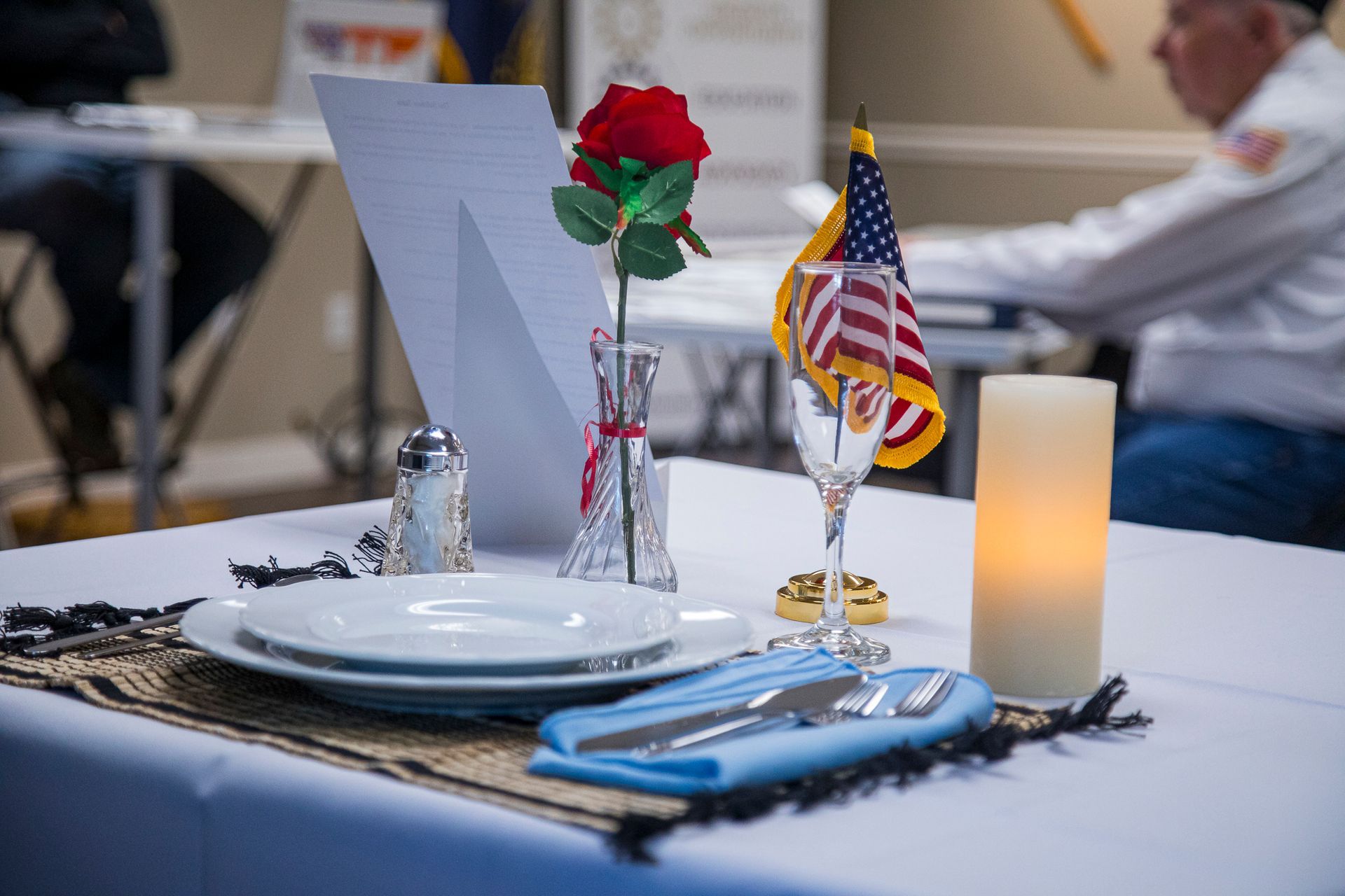 A table with plates , utensils , a candle and a rose on it.