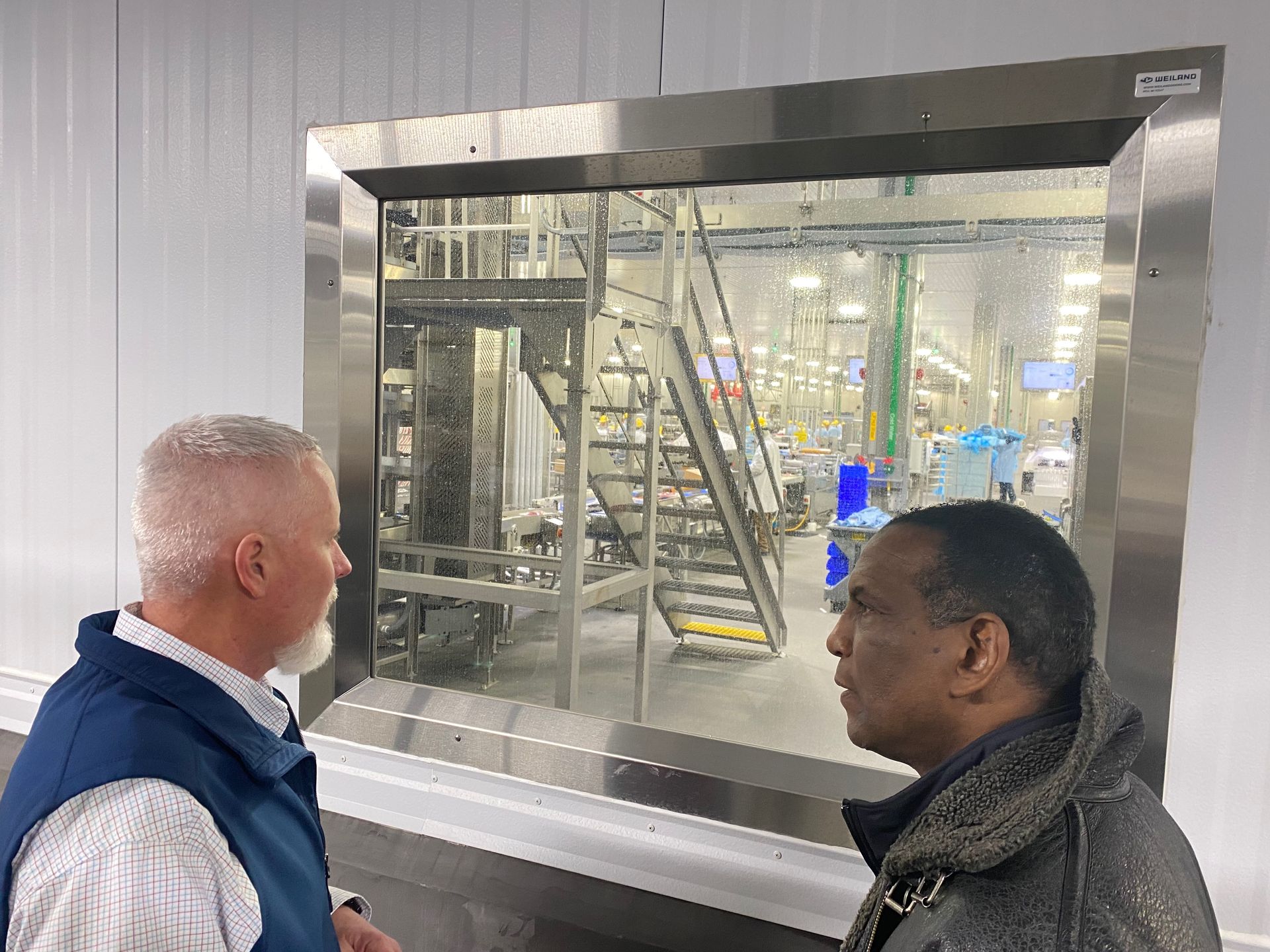 Two men are looking out of a window at a factory.