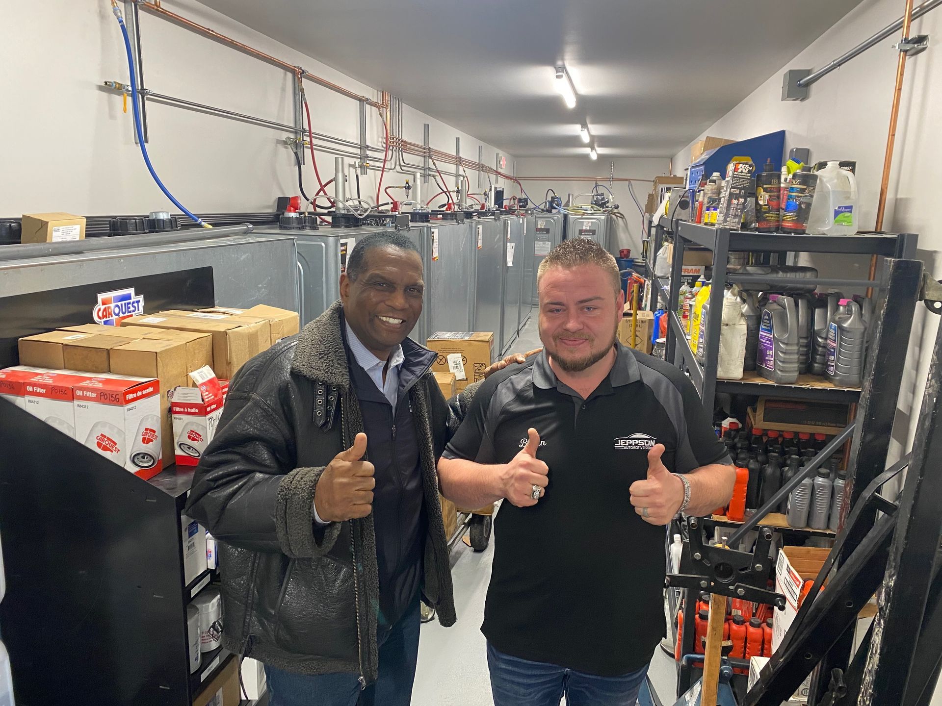 Two men are giving a thumbs up in a garage.