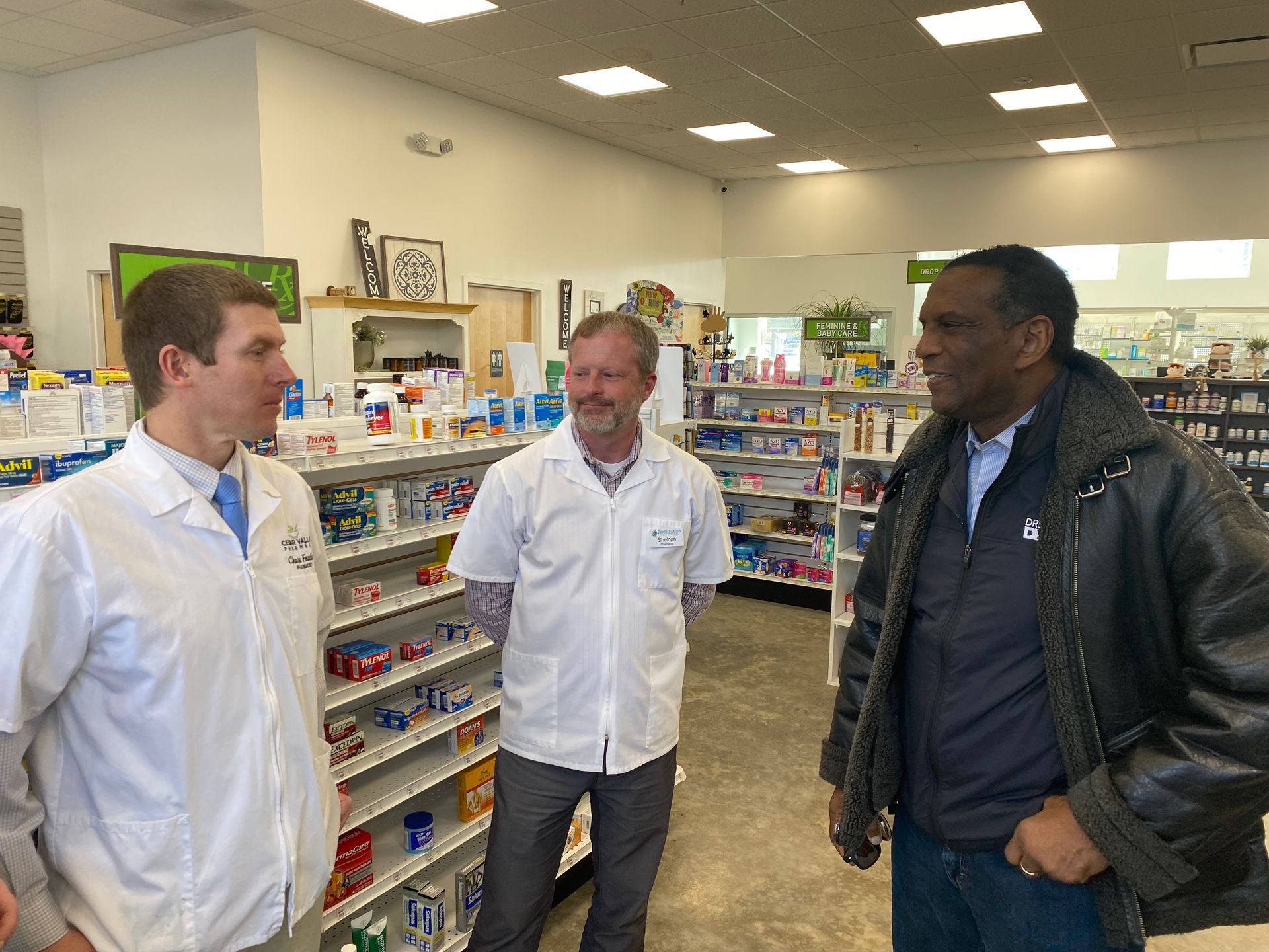Three men are standing in a pharmacy talking to each other