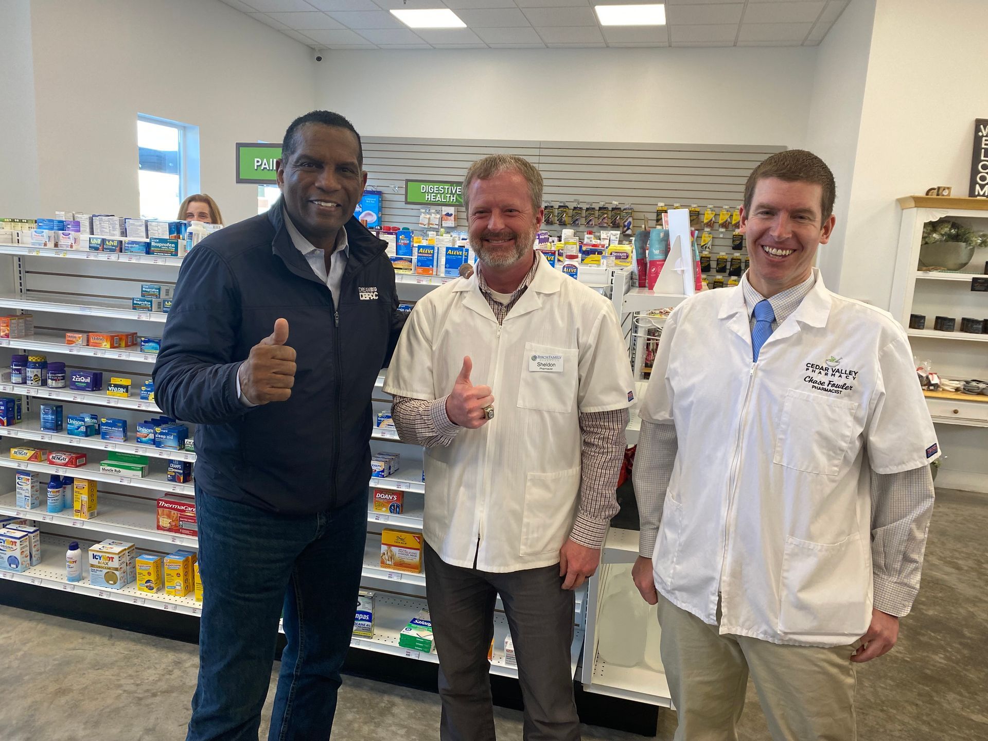 Three men are standing in a pharmacy giving a thumbs up.