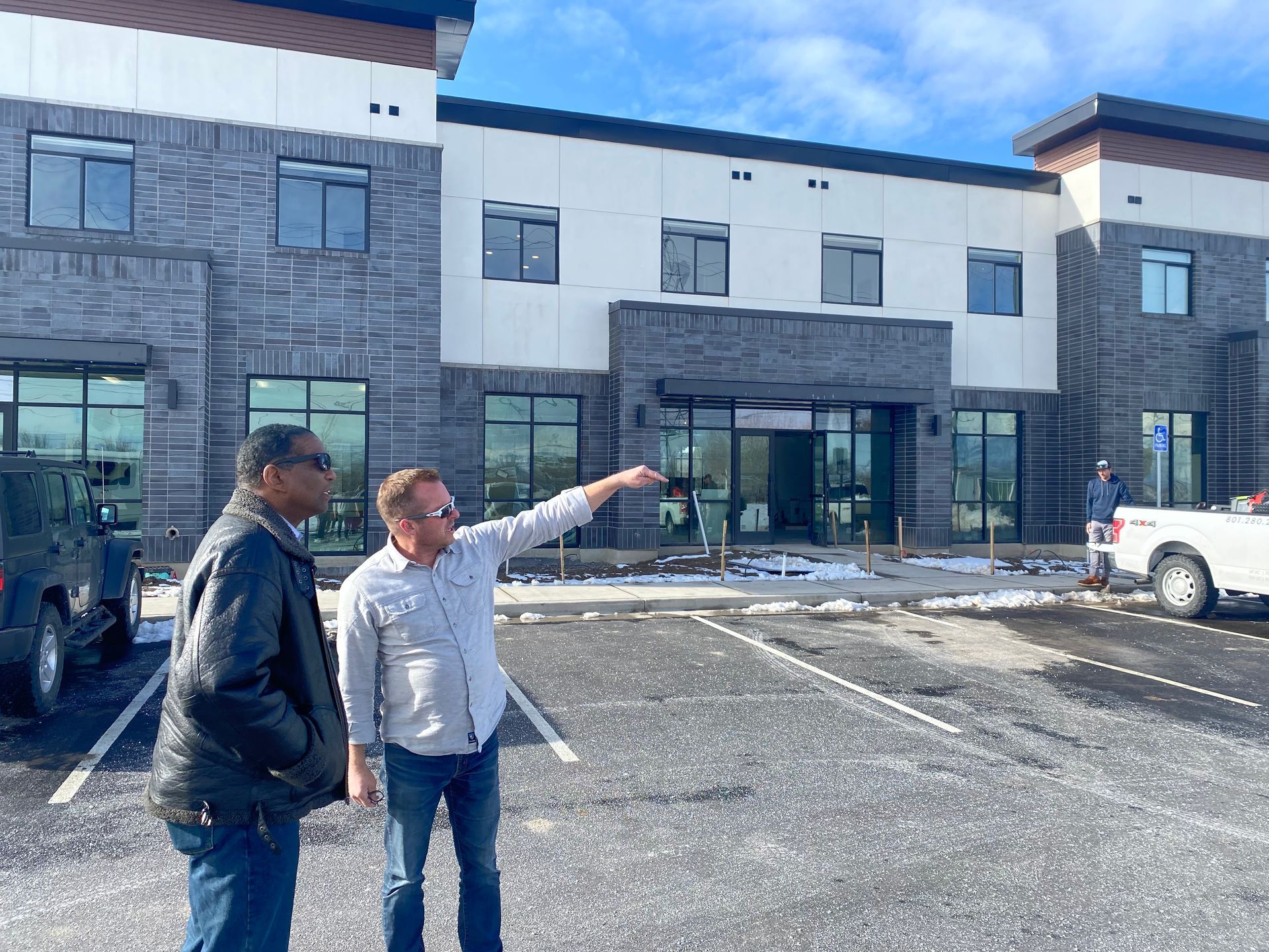 Two men are standing in front of a large building in a parking lot.