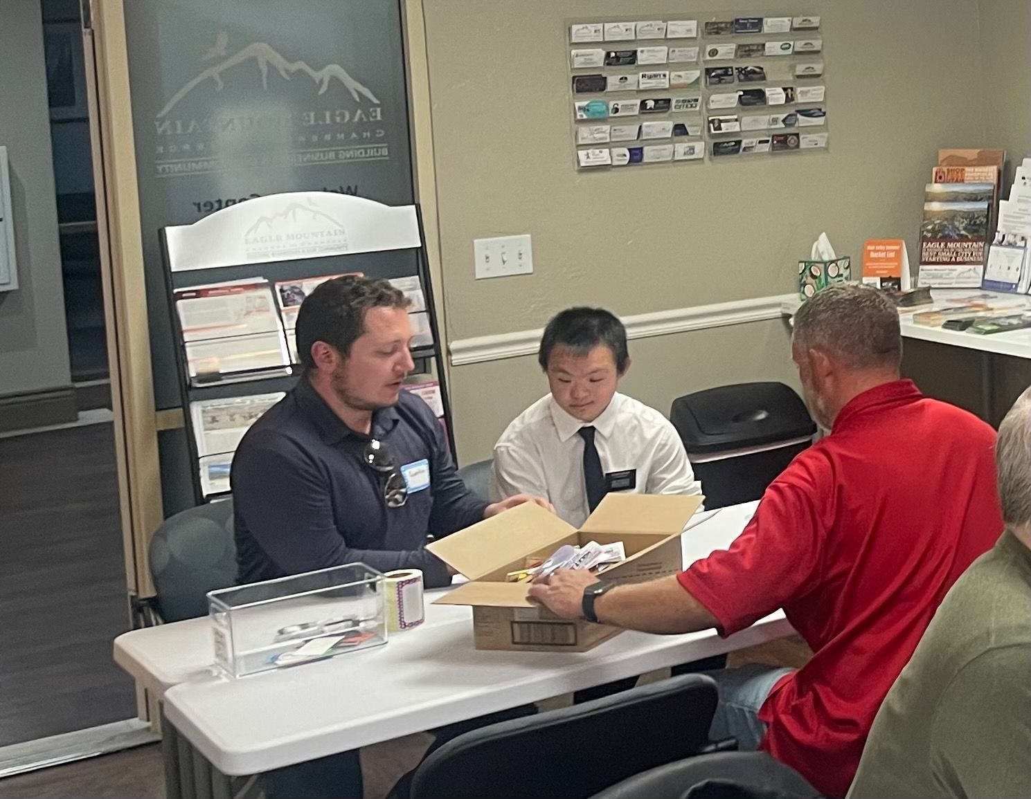 A group of men are sitting around a table looking at a box.