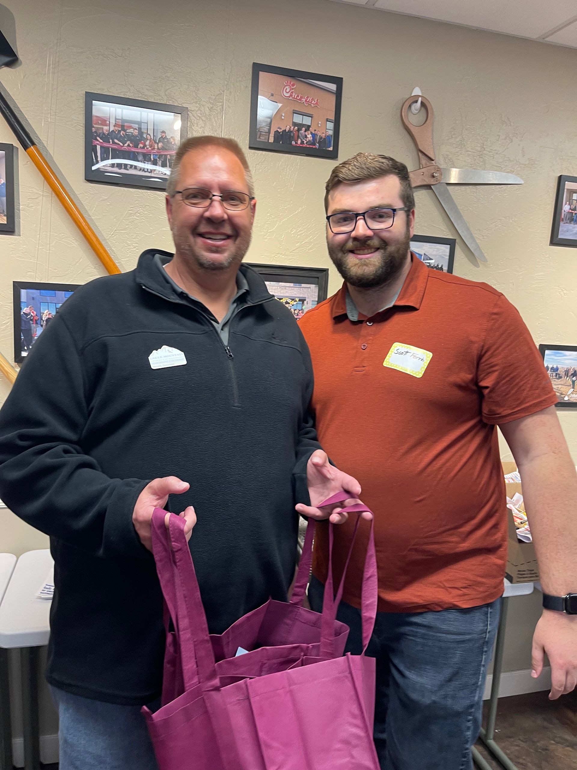 Two men are standing next to each other holding pink bags.