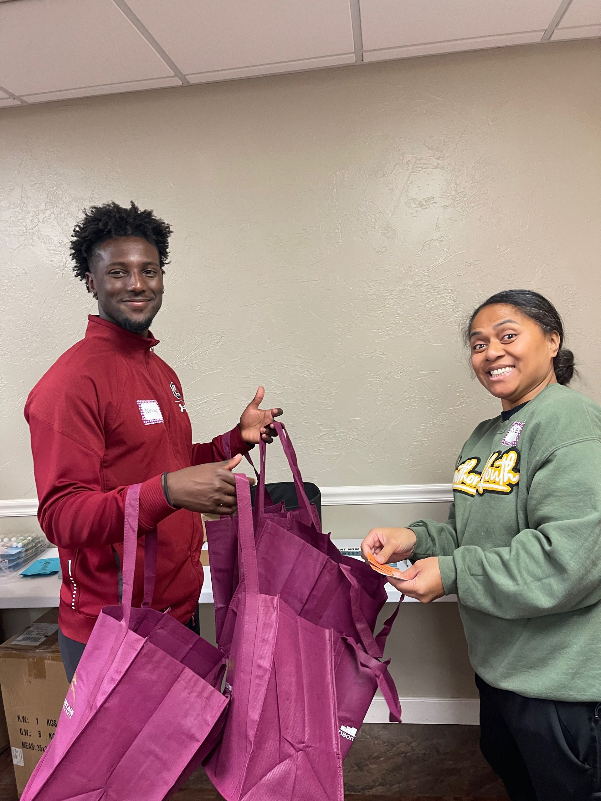A man and a woman are holding purple bags in a room.