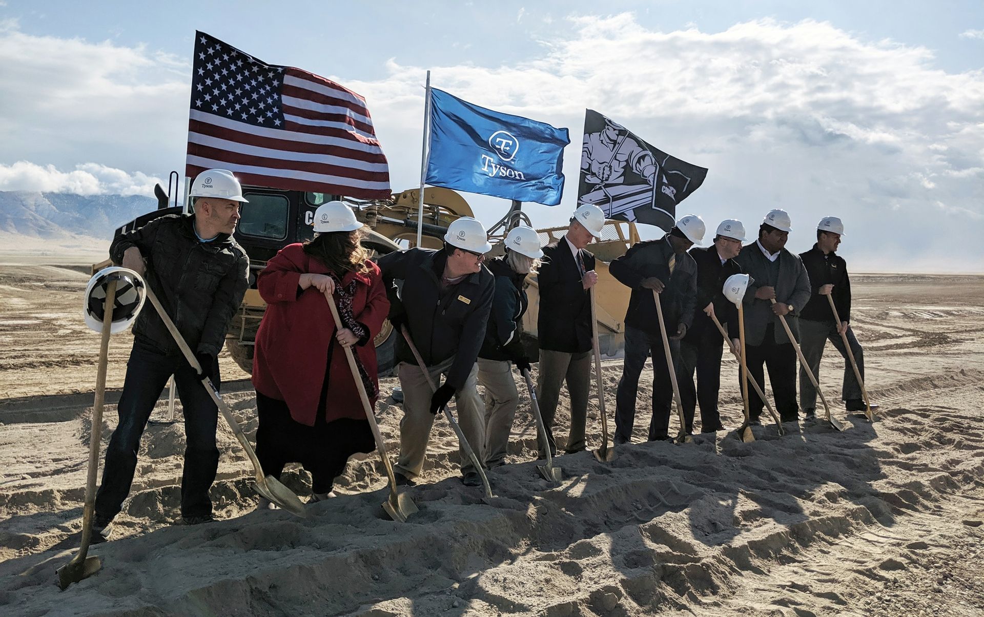 A group of people are standing in the sand holding shovels and flags.