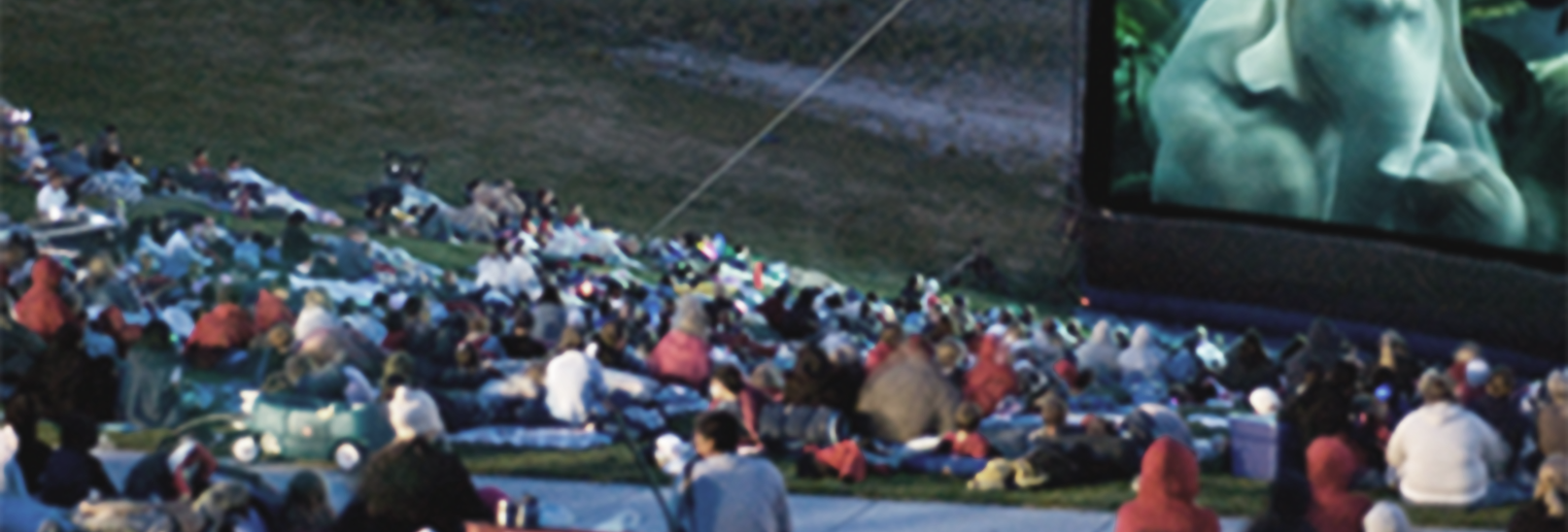 A crowd of people are watching a movie on a large screen.