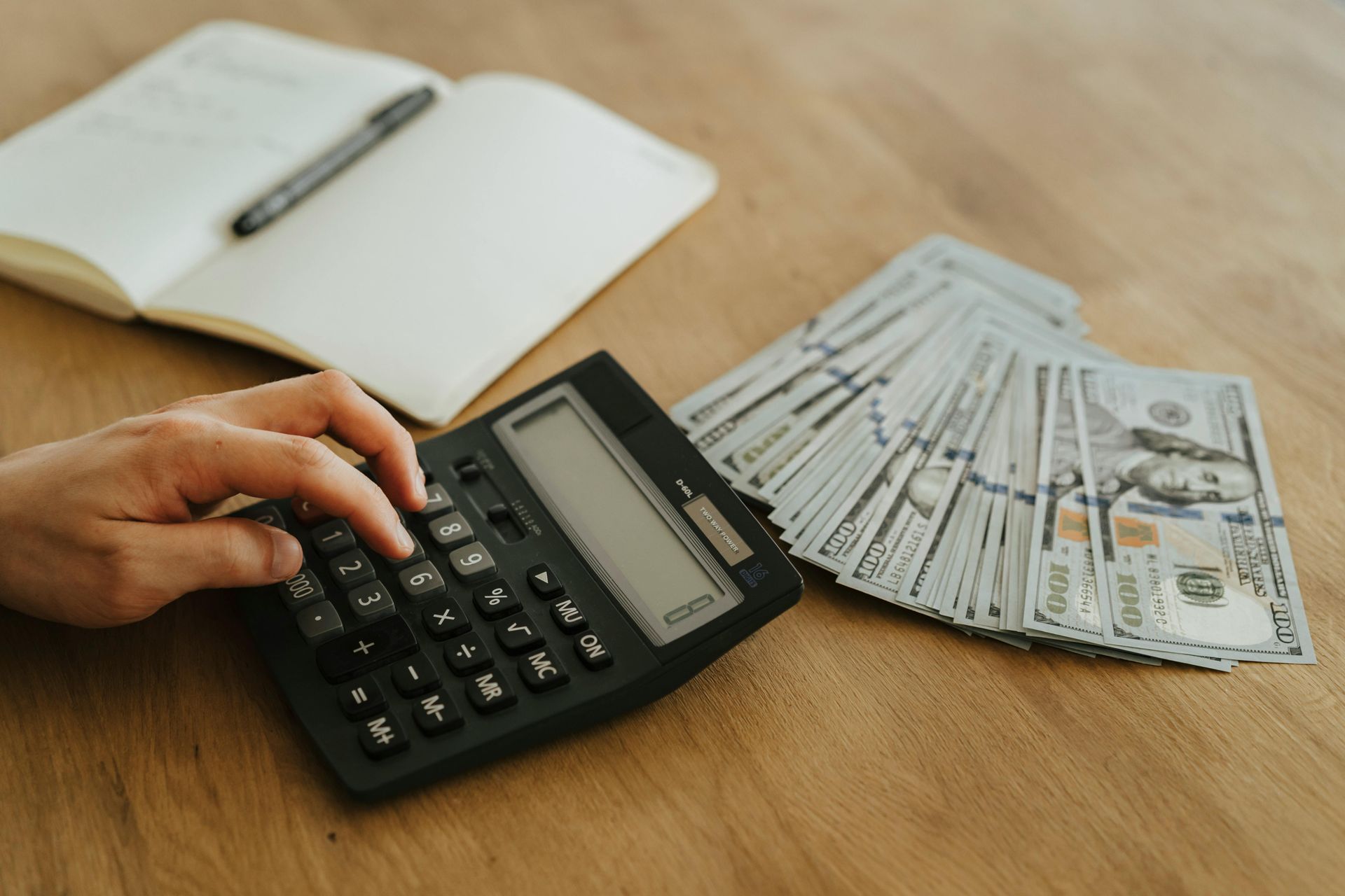 A person is using a calculator next to a pile of money.