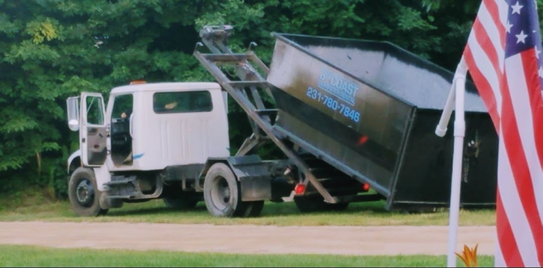 White truck lifting a black dumpster. American flag in the foreground.