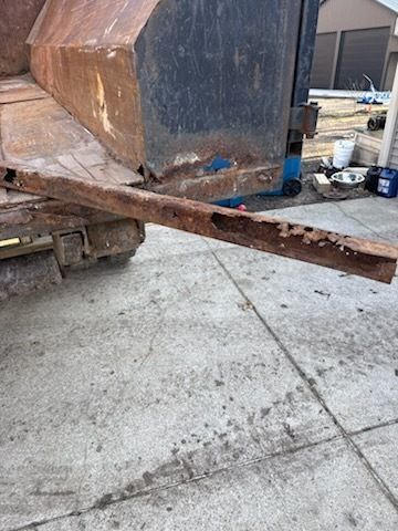 Rusty metal beam supporting a large dumpster on a concrete lot