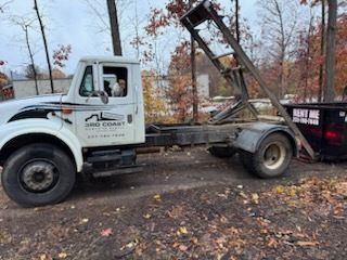White tow truck with raised hoist parked on a leaf-covered roadside in autumn.