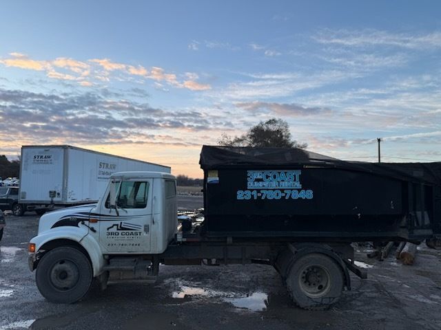 Black dump truck parked in a lot at sunset, with a white truck in the background.