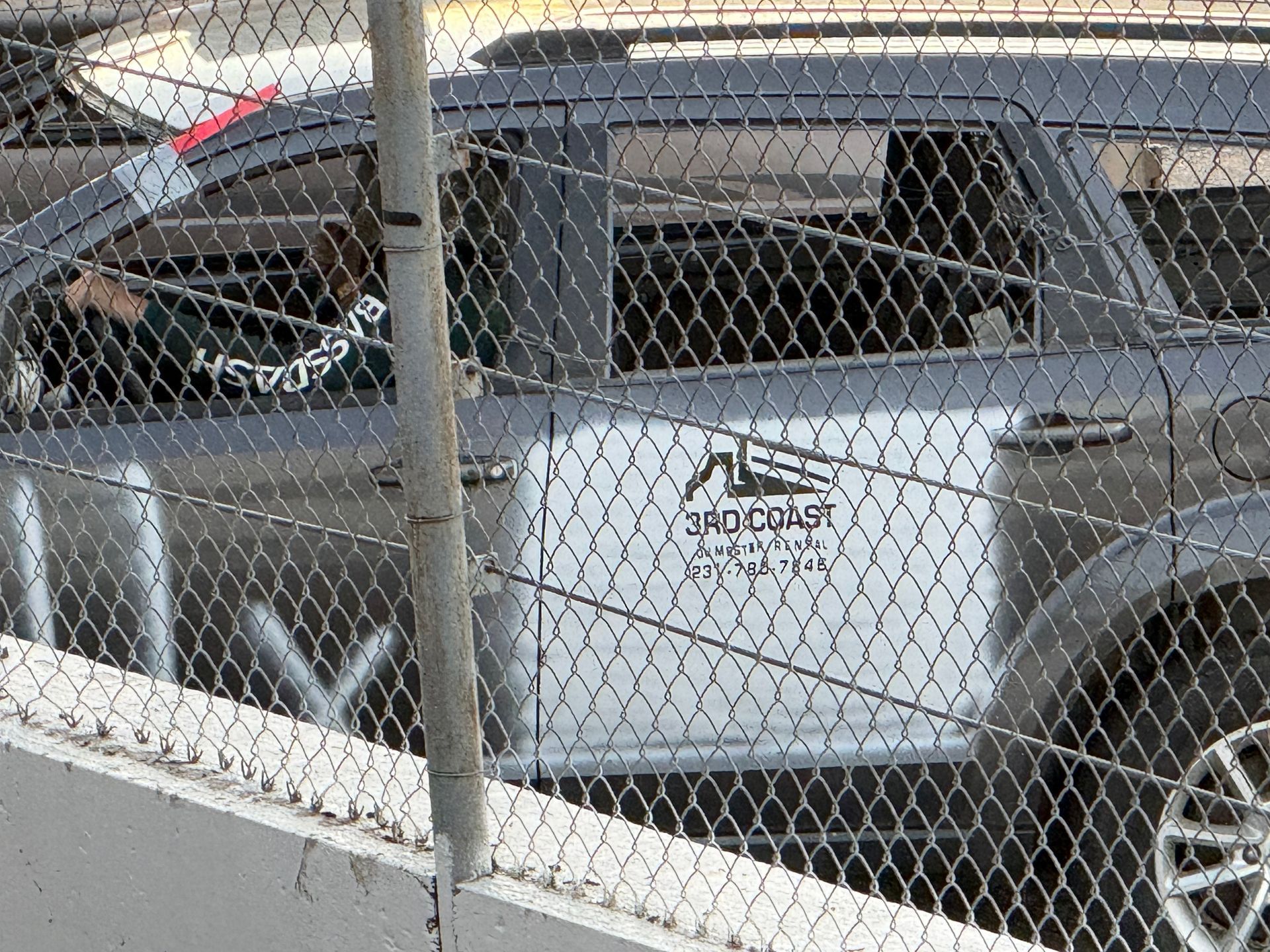 Silver SUV behind a chain-link fence with a logo on the rear door