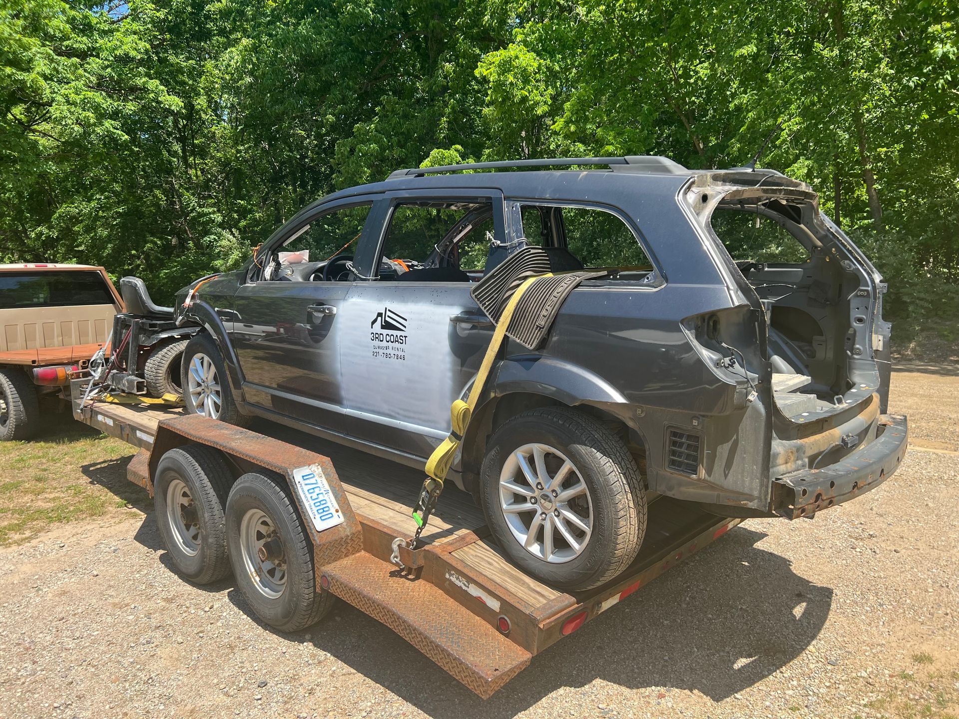 Damaged silver SUV strapped to a trailer in a grassy yard, rear hatch open and rear body missing