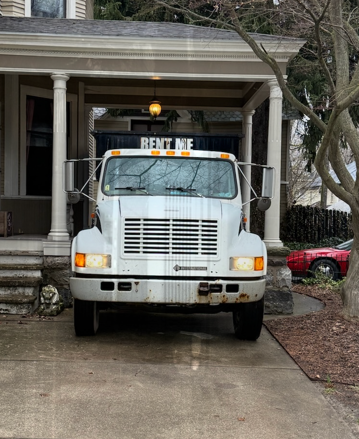 White rental truck parked in a driveway under a porch, with a lit “RENT ME” sign on top.