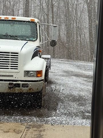 White truck parked on a snowy road in a leafless winter forest as snow falls