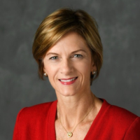A woman wearing a red jacket and a gold necklace smiles for the camera
