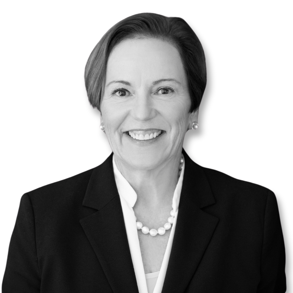 A woman in a suit and pearl necklace is smiling in a black and white photo.