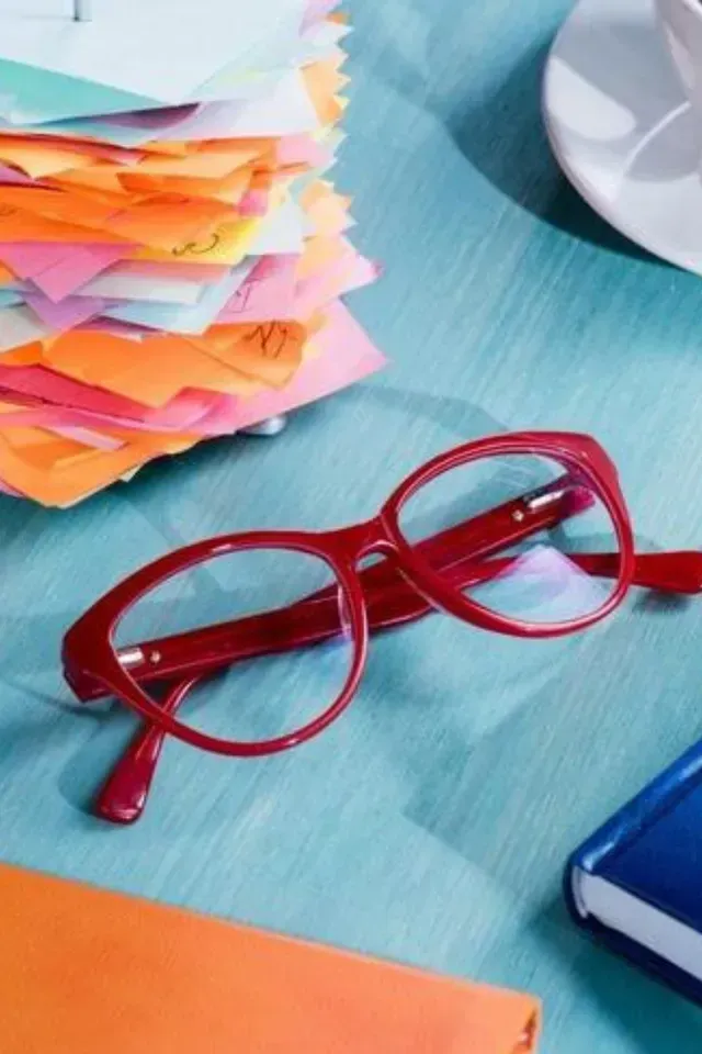 A pair of red glasses sits on a table next to a stack of sticky notes