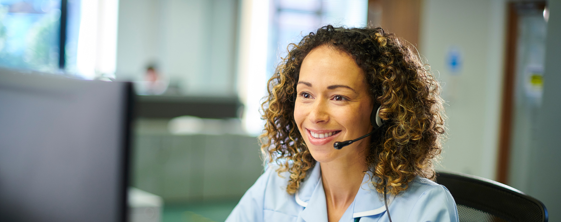 A nurse wearing a headset is sitting in front of a computer.