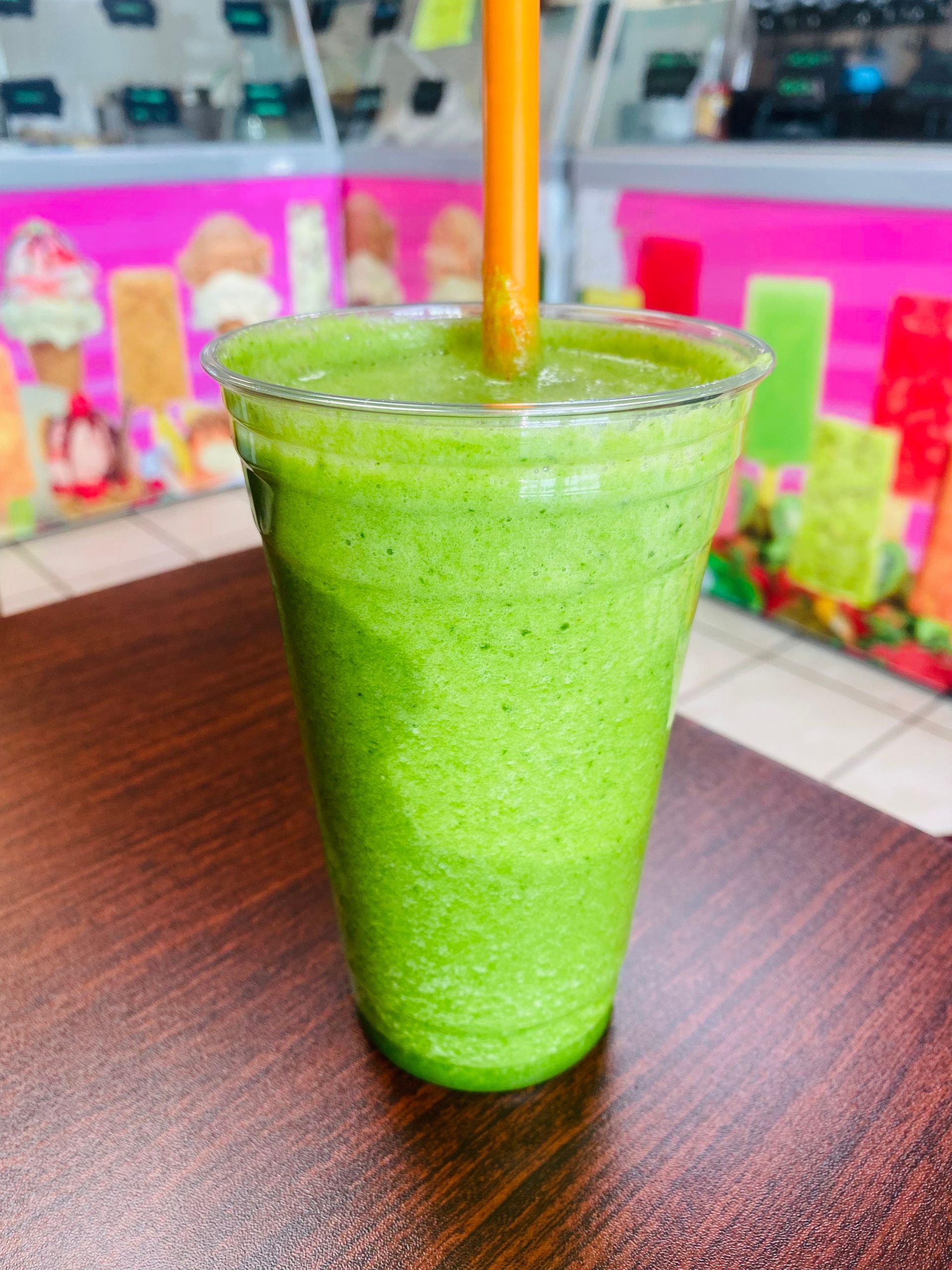 A green smoothie with a straw in it is sitting on a wooden table.