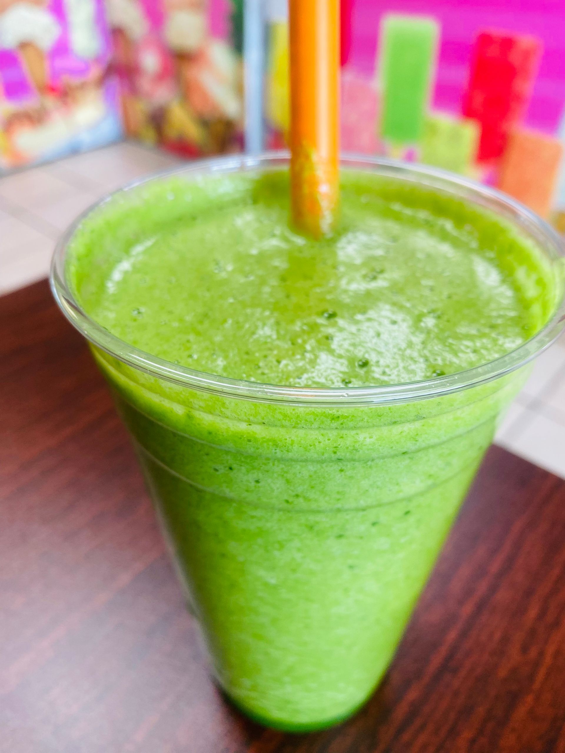 A green smoothie with a straw in it is sitting on a wooden table.