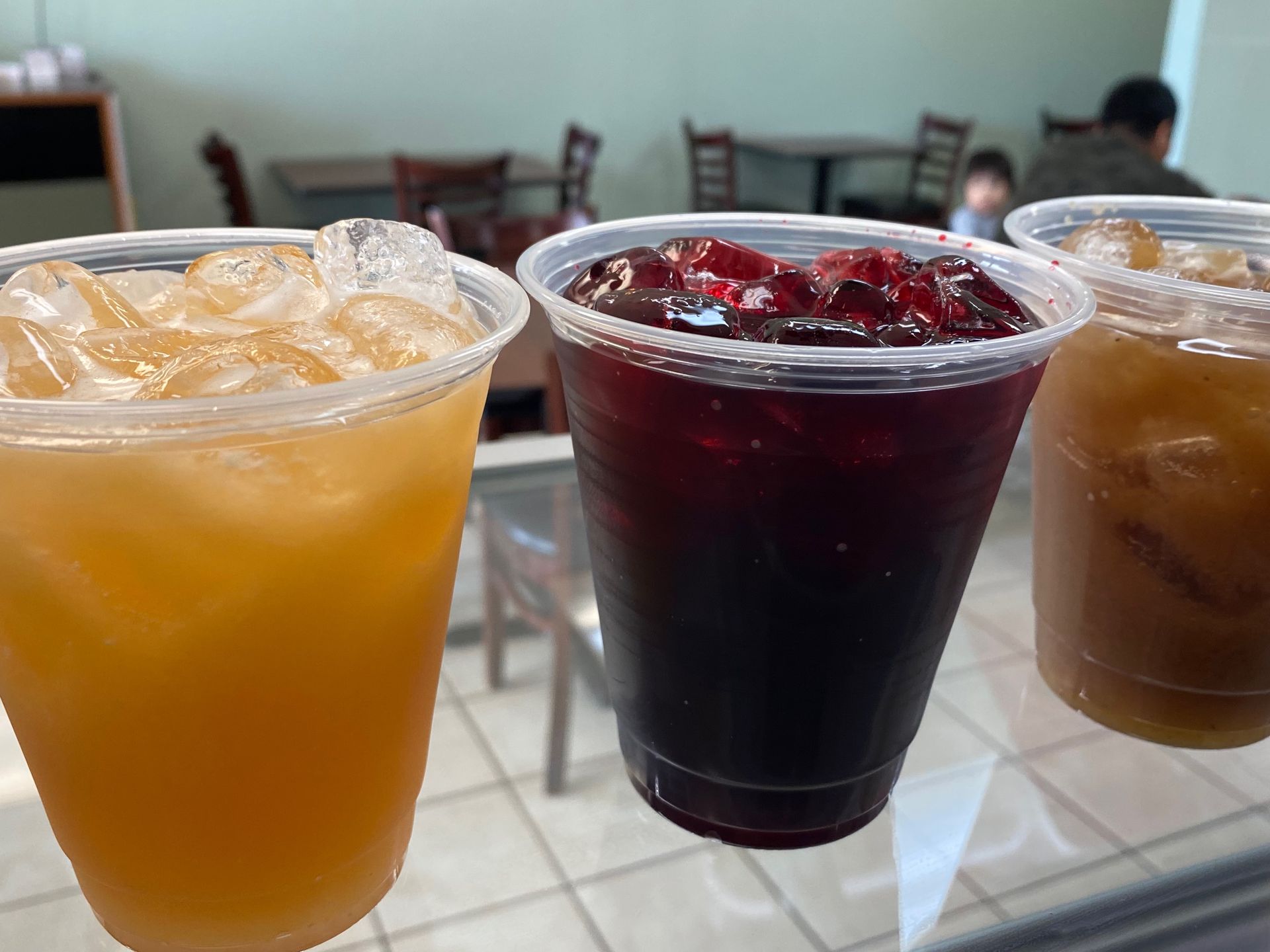 Three cups of iced tea are sitting on a glass shelf in a restaurant.