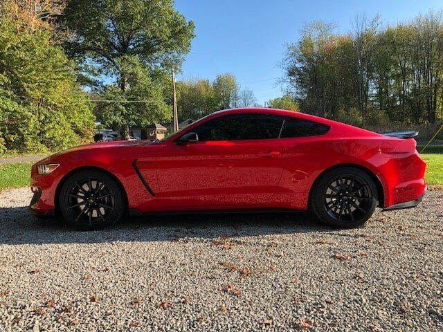 A red ford mustang is parked on a gravel road.