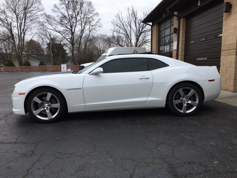 A white car is parked in a parking lot in front of a garage.