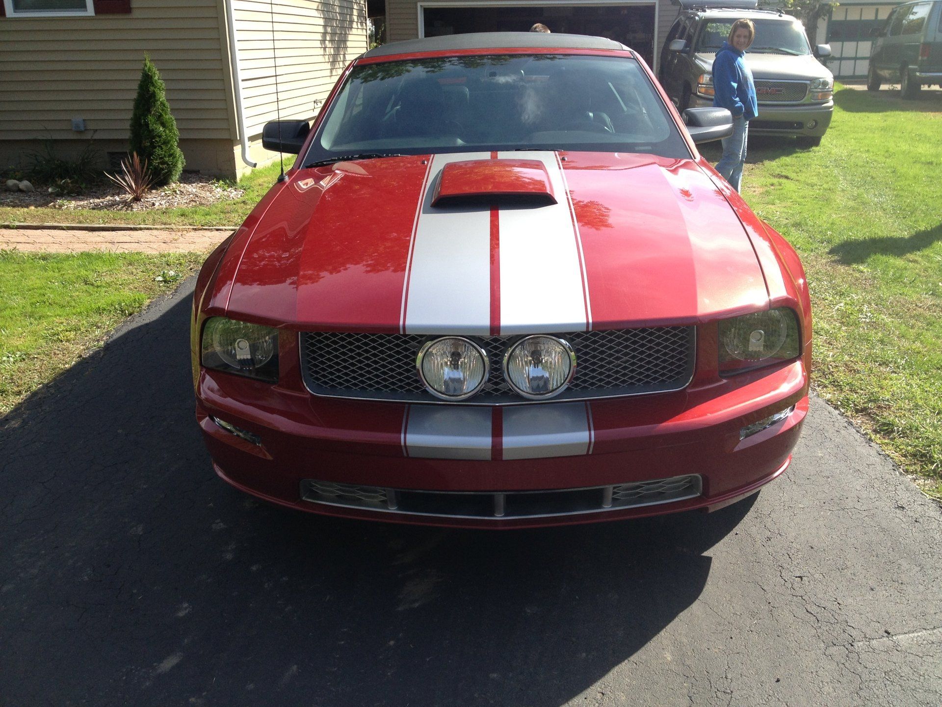 A red mustang with white stripes on the hood is parked in a driveway