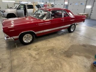 A red car is parked in a garage next to a truck.
