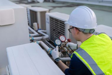 Technician in hard hat inspecting pressure gauges on rooftop HVAC pipes