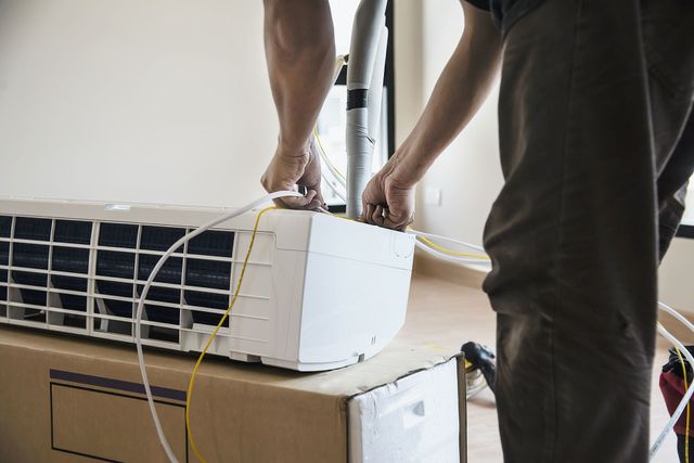 Person handling a portable air conditioner with wires, indoors near a window