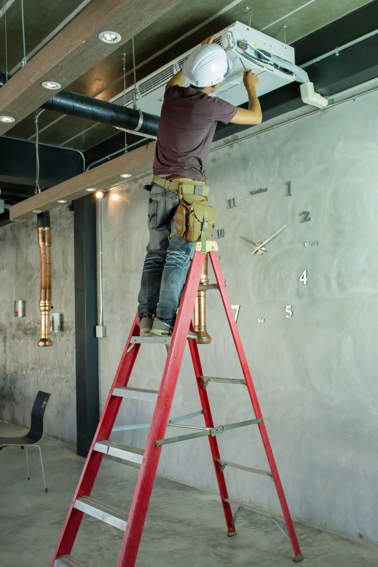 Worker on a red ladder installing ceiling fixtures in an unfinished room