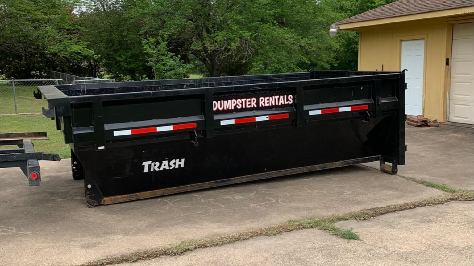 A dumpster is parked in a driveway next to a house.
