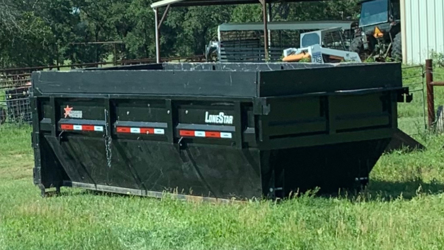 A dumpster is sitting in the middle of a grassy field.