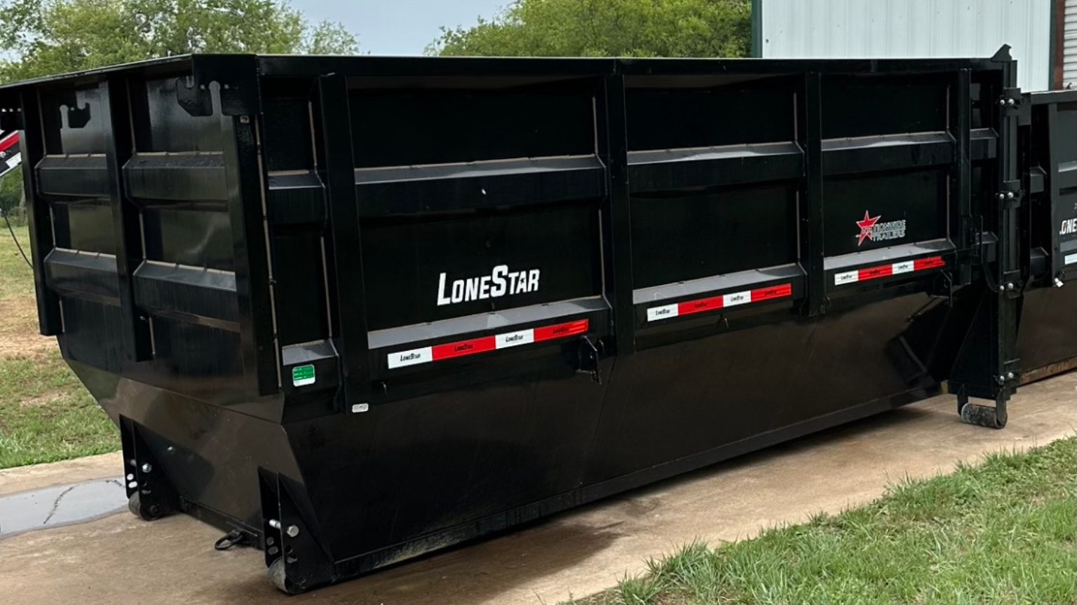 A large black dumpster is parked on the side of the road.