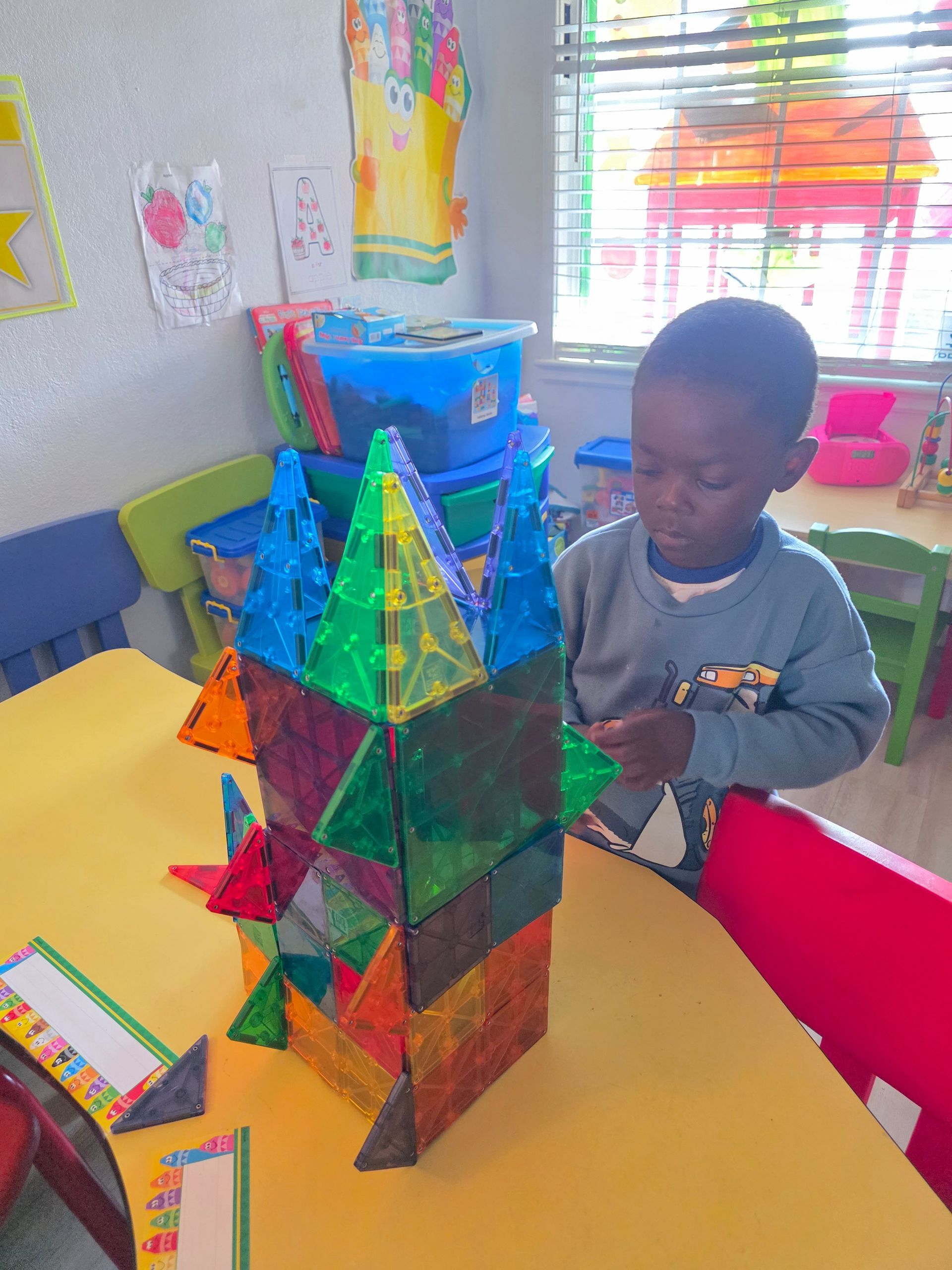 Young child building with colorful magnetic tiles at a table.