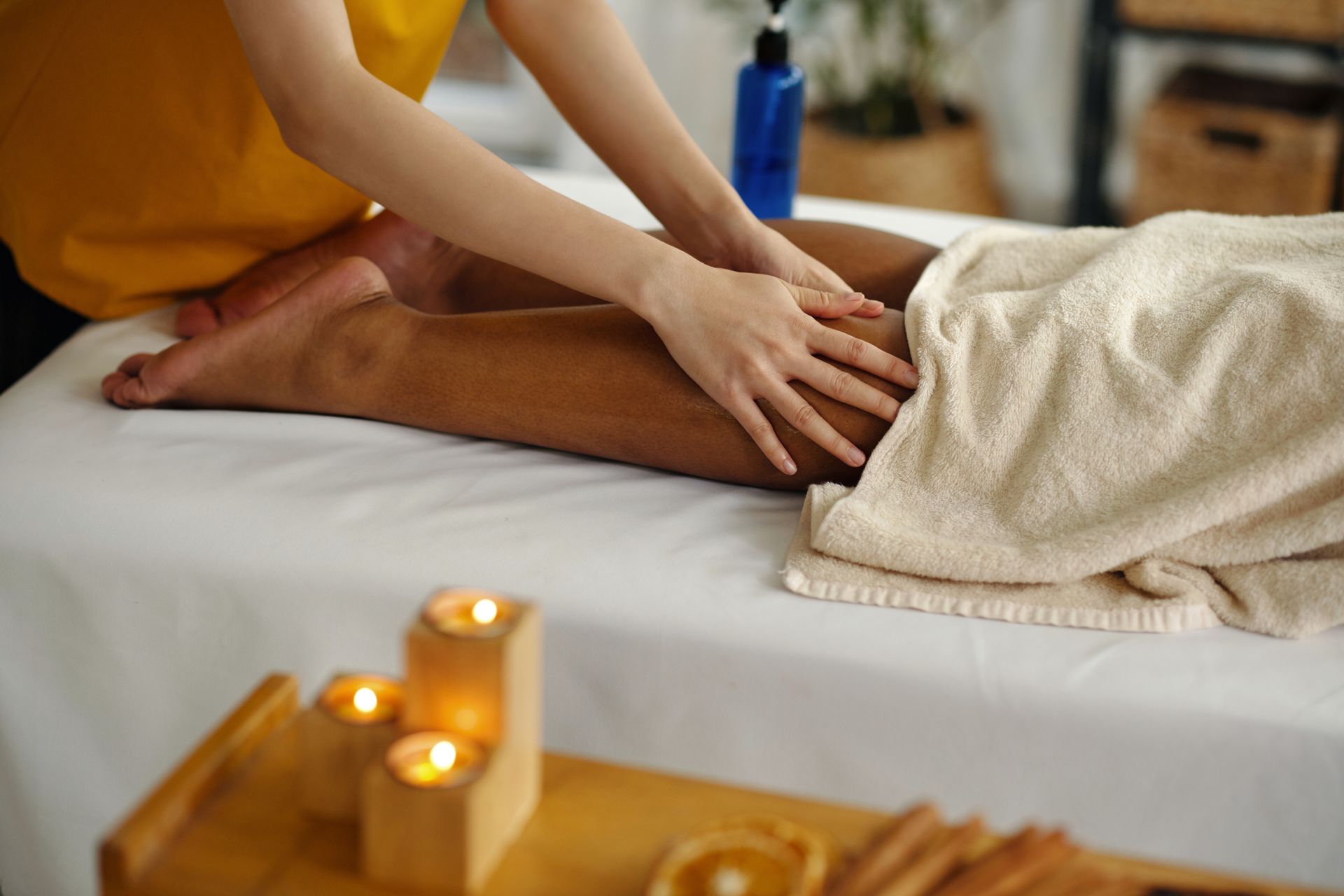 Massage therapist rubbing a client’s leg on a treatment table with candles nearby