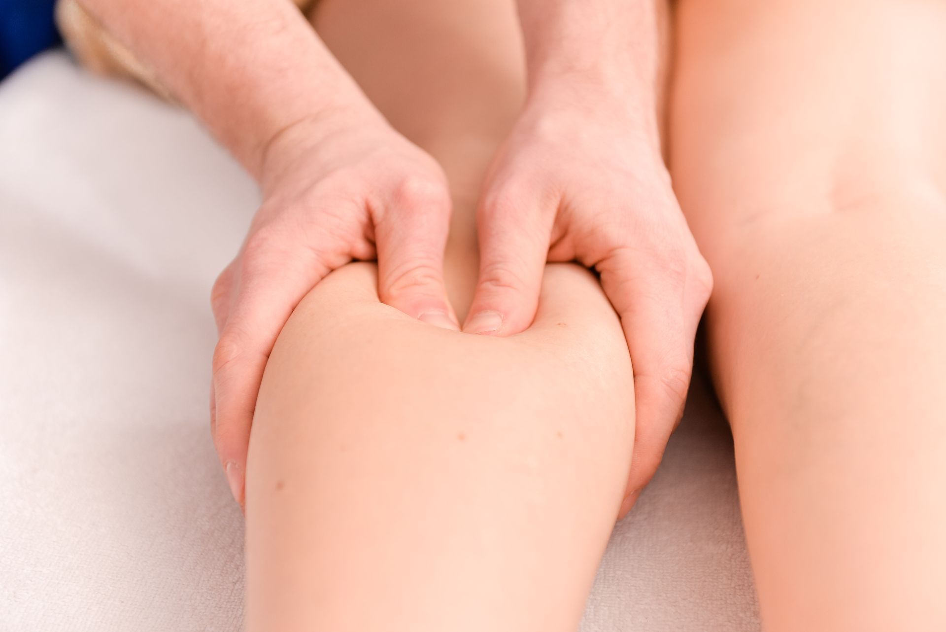 Hands gently massaging a person's knee against a light background