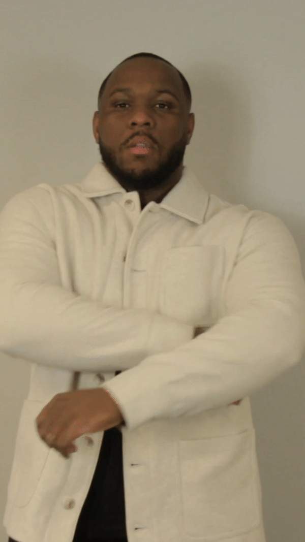 A man with a beard is wearing a white jacket with his arms crossed