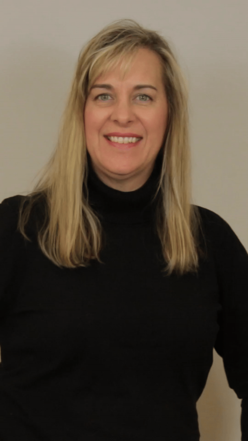 A woman wearing a black jacket and a red shirt is smiling for the camera.