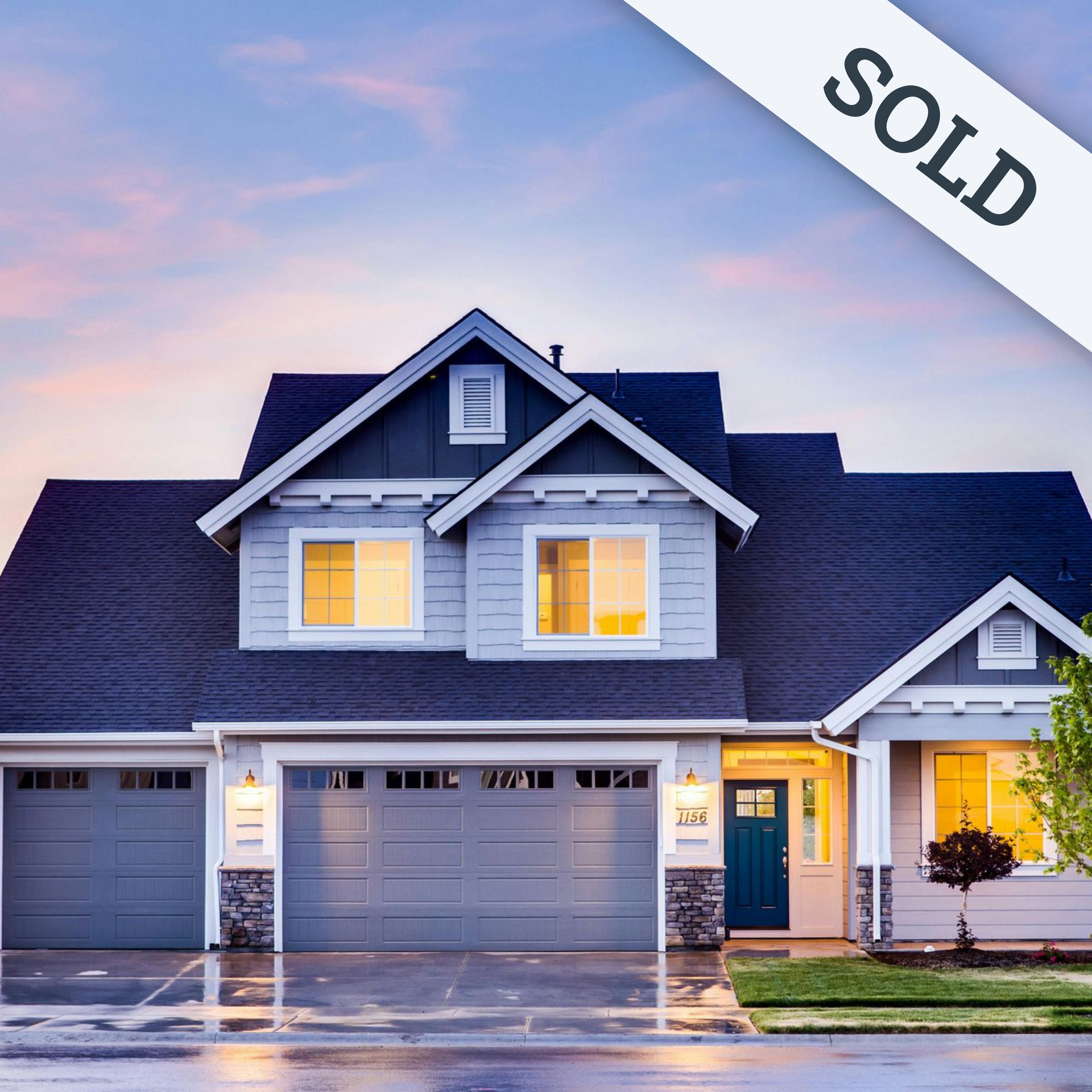 A large house with a blue roof and two garage doors is lit up at night.